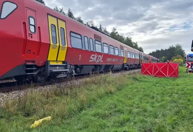 Czerwony pociąg SKPL stoi na torach w zalesionym terenie, a obok kolei ustawiono czerwony parawan ratowniczy i widać pojazd służb.